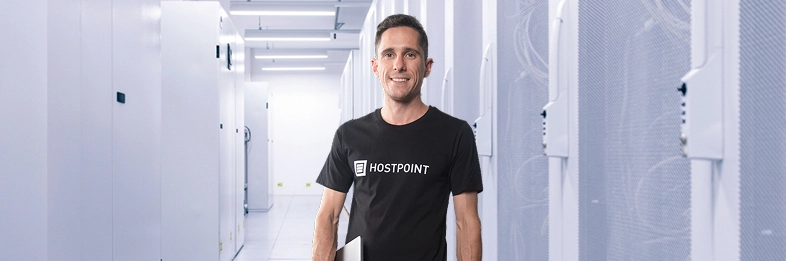 Homme portant un t-shirt Hostpoint et un ordinateur portable sous le bras, debout dans un centre de données.